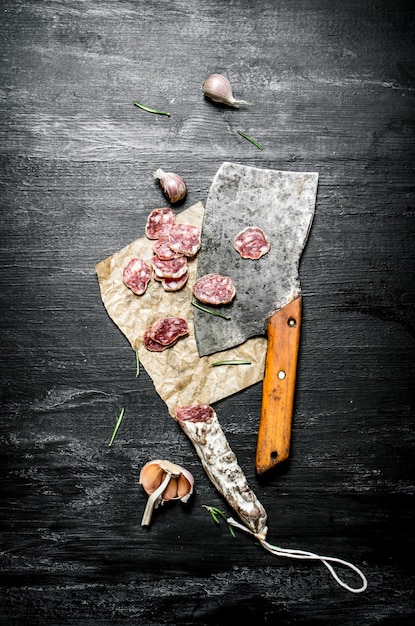 Salami met knoflook en een oude bijl. Op zwarte rustieke achtergrond.