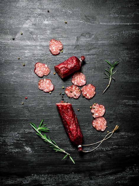 Salami met verse rozemarijn en kruiden op zwarte rustieke tafel.