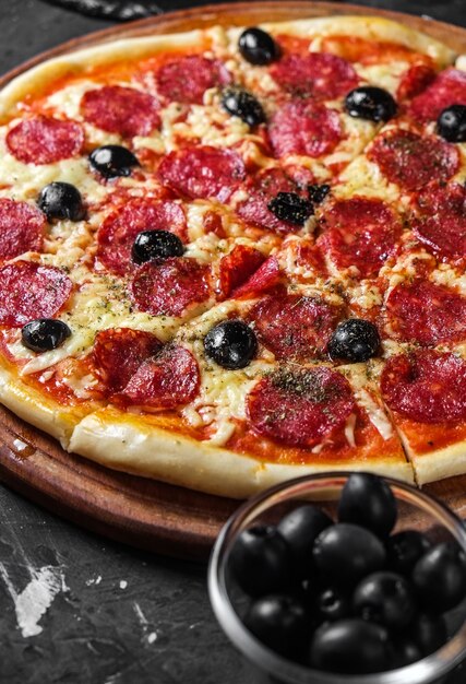 Salami pizza with olives on a dark surface