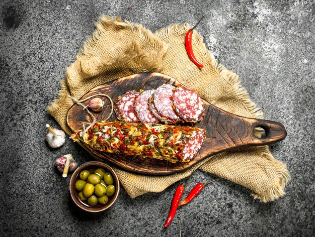 Salame di maiale e manzo con olive e spezie su fondo rustico