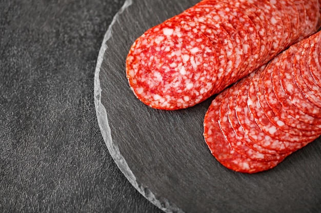 Salami sausage meat with bacon cut into circles closeup on slate stone plate round dark background top view selective focus