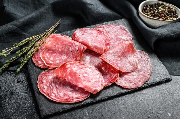 Salami sausage slices on a black chopping Board. Dark background. Top view