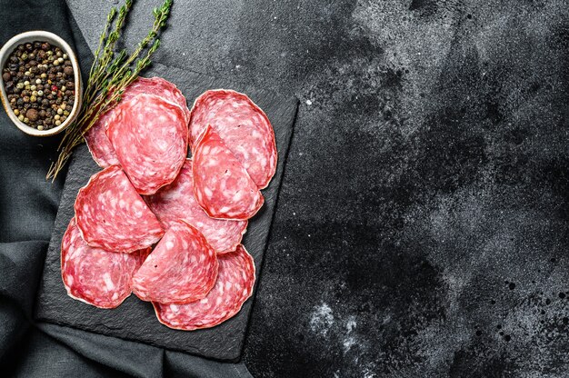 Salami sausage slices on a black chopping Board. Dark background