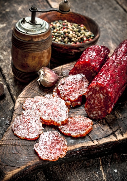 Salami with herbs and spices on a board. On a wooden background.