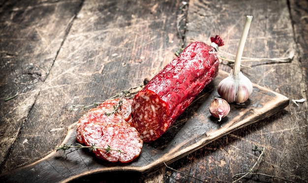 Salami with herbs and spices on a board on a wooden background