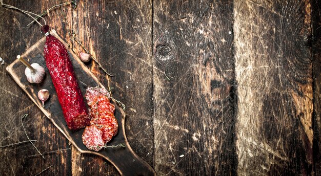 Salami with herbs and spices on a board on a wooden background