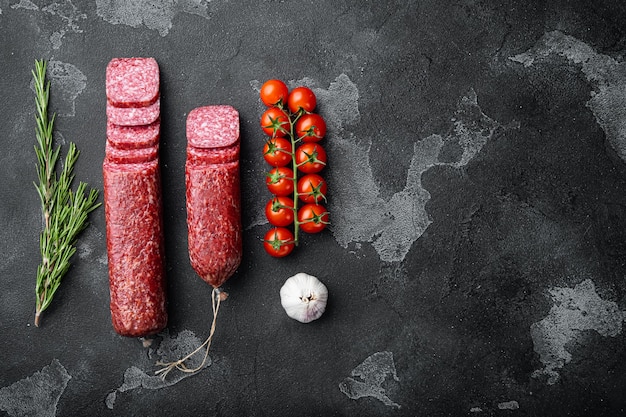 Salami with herbs and spices set, on black dark stone table, top view flat lay