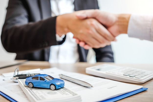 Affare della stretta di mano dell'agente di vendita per concordare il riuscito contratto di prestito dell'automobile con il cliente e firmare il concetto dell'automobile dell'assicurazione del contratto di accordo.