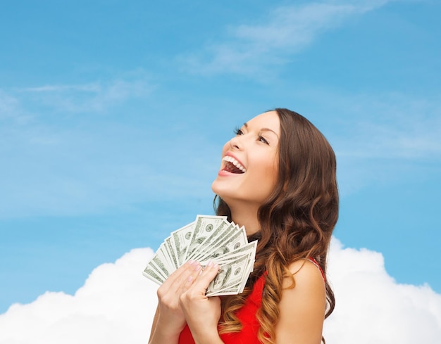 sale, banking and people concept - smiling woman in red dress with us dollar money over blue sky with white cloud background