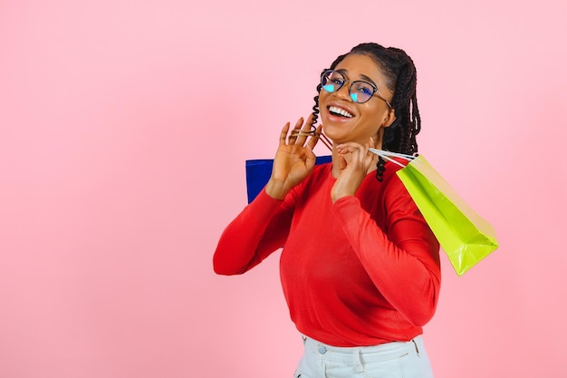 Концепция продажи Возбужденная афро девушка, держащая щеку и сумки с покупками, смотрит в сторону с открытым ртом на розовой стене copyspace