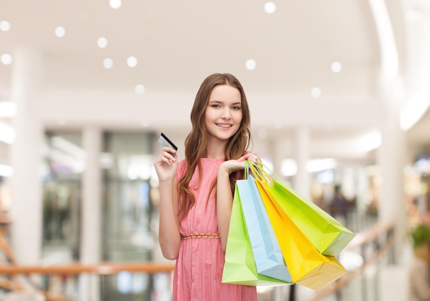 판매, 소비주의, 돈, 사람 개념 - 쇼핑몰에서 쇼핑백과 신용 카드를 가진 행복한 젊은 여성