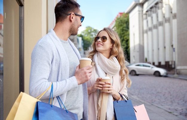 sale, consumerism and people concept - happy couple with shopping bags and coffee paper cups at shop window in city