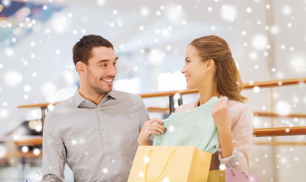 sale, consumerism and people concept - happy young couple showing content of shopping bags in mall with snow effect