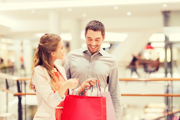 Foto vendita, consumismo e concetto di persone - giovane coppia felice che mostra il contenuto delle borse della spesa nel centro commerciale