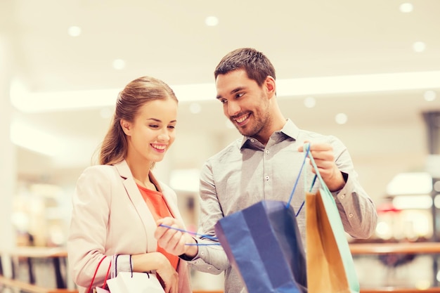 Sale, consumerism and people concept - happy young couple showing content of shopping bags in mall