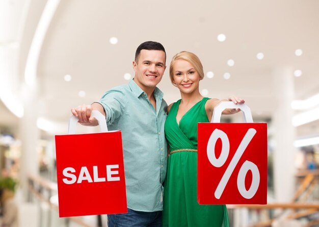 sale, consumerism and people concept - happy young couple with red shopping bags in mall