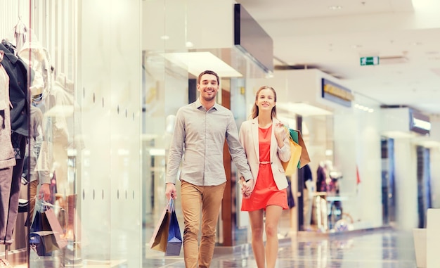 sale, consumerism and people concept - happy young couple with shopping bags walking in mall