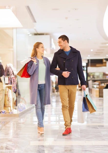 продажа, потребительство и концепция людей - счастливая молодая пара с сумками для покупок ходит и разговаривает в торговом центре