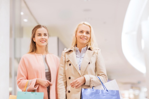 sale, consumerism and people concept - happy young women with shopping bags in mall