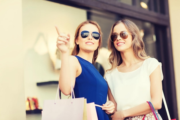 Foto vendita, consumismo e concetto di persone - giovani donne felici con borse della spesa che puntano il dito alla vetrina del negozio in città