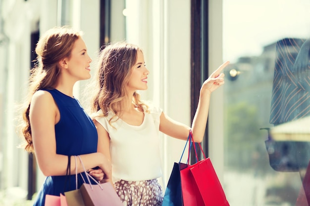 판매, 소비주의, 사람 개념 - 쇼핑백을 들고 도시의 쇼핑 창을 가리키는 행복한 젊은 여성
