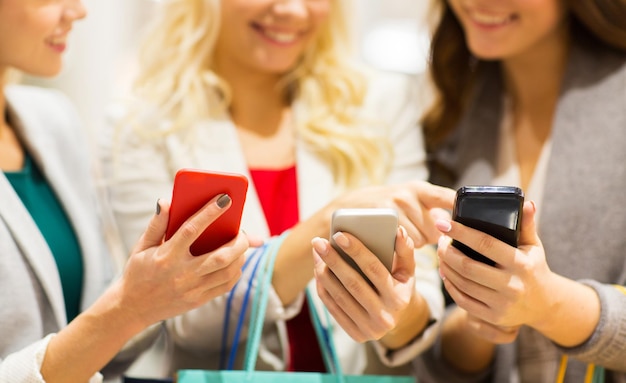 Foto concetto di vendita, consumismo, tecnologia e persone - giovani donne felici con smartphone e borse della spesa che parlano nel centro commerciale