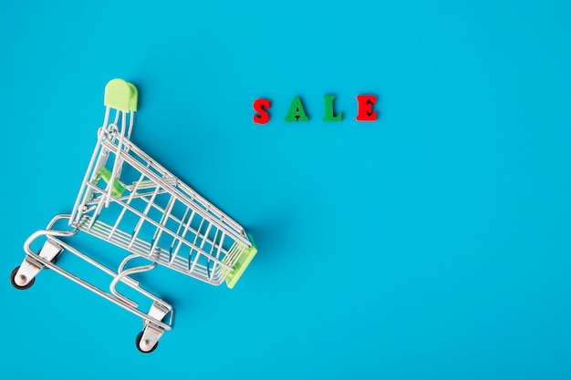 Sale and discounts concept supermarket trolley and letters on a\
blue background with copy space