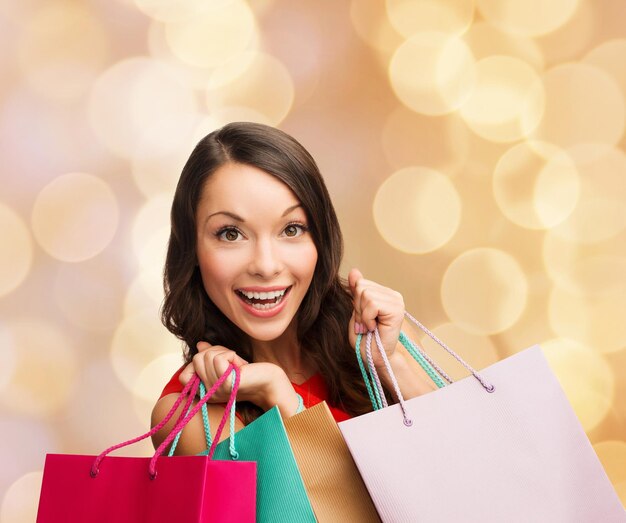 sale, gifts, christmas, holidays and people concept - smiling woman with colorful shopping bags over beige lights background