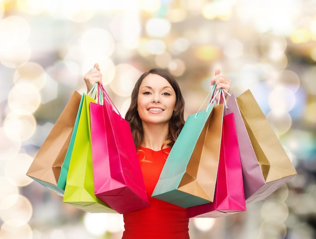 판매, 선물, 크리스마스, 휴일 및 사람 개념 - 조명 배경 위에 화려한 쇼핑백을 들고 웃는 여자