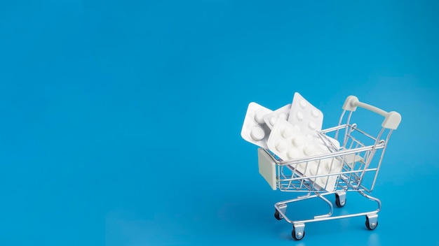 Sale of medical drugs online via the Internet tablets in a cart trolley on a blue background with copy space