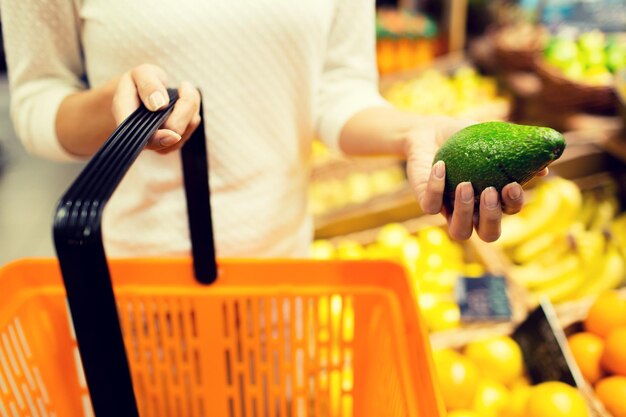 販売、ショッピング、消費、人々 のコンセプト - 市場で食品バスケットとアボカドを持つ若い女性のクローズ アップ