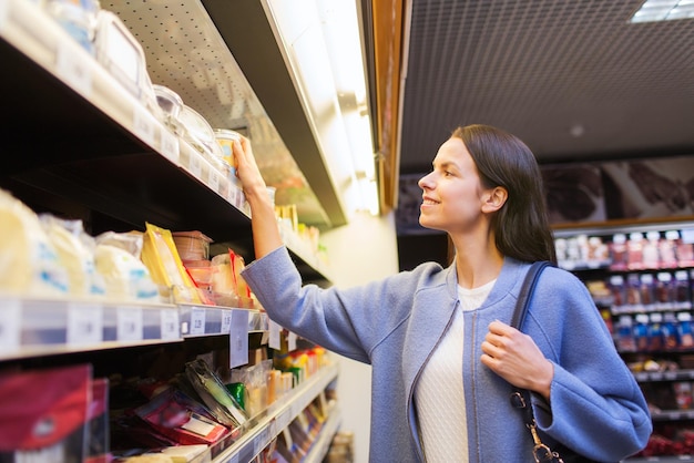 sale, shopping, consumerism and people concept - happy young woman choosing and buying food in market