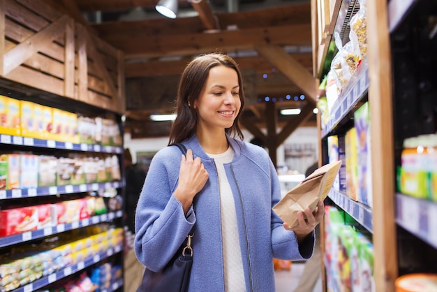 sale, shopping, consumerism and people concept - happy young woman choosing and buying food in market