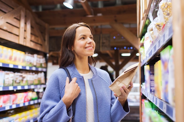 sale, shopping, consumerism and people concept - happy young woman choosing and buying food in market