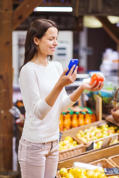 sale, shopping, consumerism and people concept - happy young woman with smartphone and tomato in market