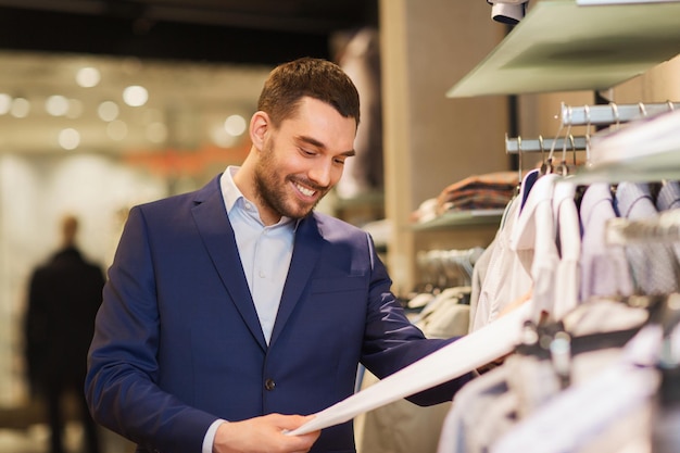 sale, shopping, fashion, style and people concept - happy elegant young man in suit choosing clothes in mall or clothing store