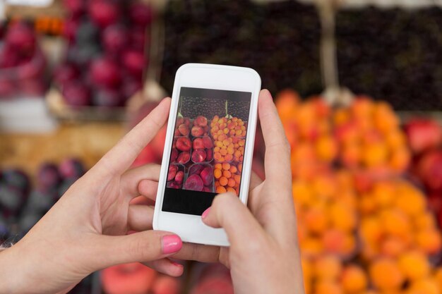 sale, shopping, food, technology and people concept - close up of hands with smartphone taking picture of fruits at street market