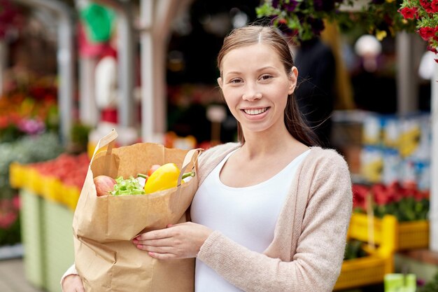 продажа, покупки и концепция людей - счастливая женщина с бумажным пакетом, полным еды на уличном рынке