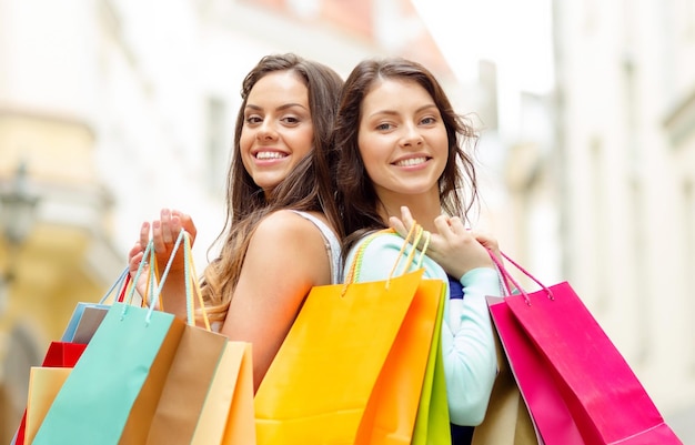 sale, shopping, tourism and happy people concept - two beautiful women with shopping bags in the ctiy