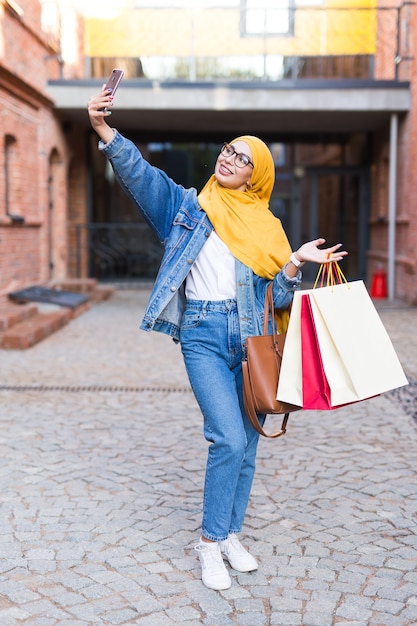 Продажа, технологии и концепция покупки - Счастливая арабская мусульманская женщина, делающая селфи на открытом воздухе после
