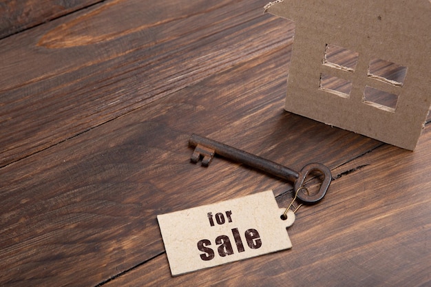 For sale text on the key label House model and old key on wooden background real estate buy or rent concept