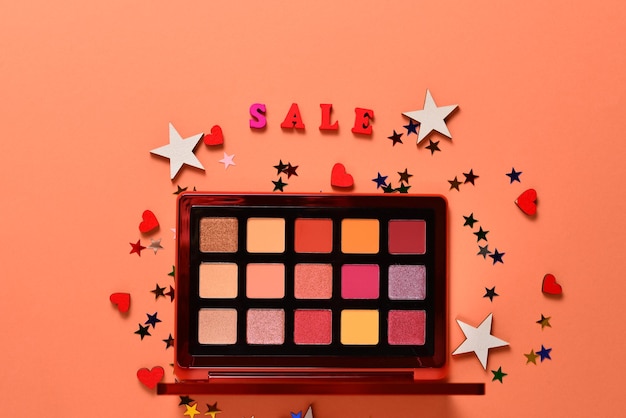 Sale text on an orange background. Professional trendy makeup products with cosmetic beauty products,  eye shadows, eye lashes, brushes and tools.