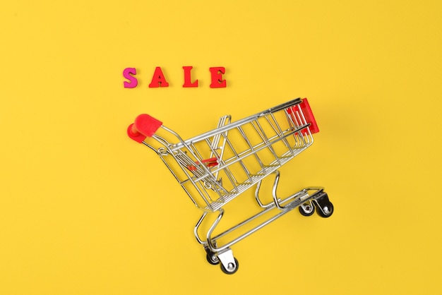 Sale text and shopping cart on a yellow surface