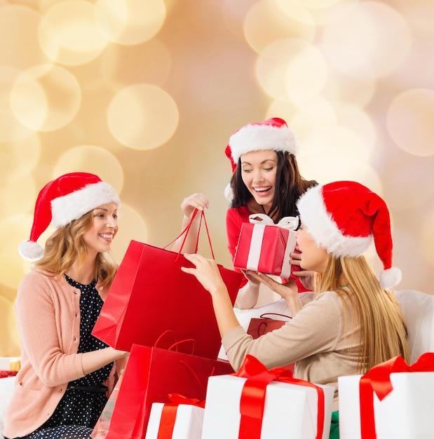 Vendita, vacanze invernali, natale e concetto di persone - giovane donna sorridente in cappello santa helper con regali e borse della spesa su sfondo di luci beige