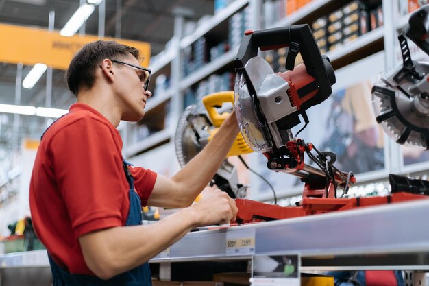 Sales assistant of a construction store stands near a shelf with power tools