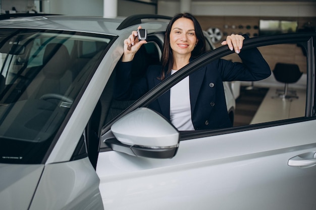 sales woman in car showroom holding car keys and standing by the car