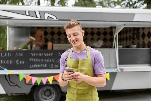 Photo salesman in apron with smartphone at food truck