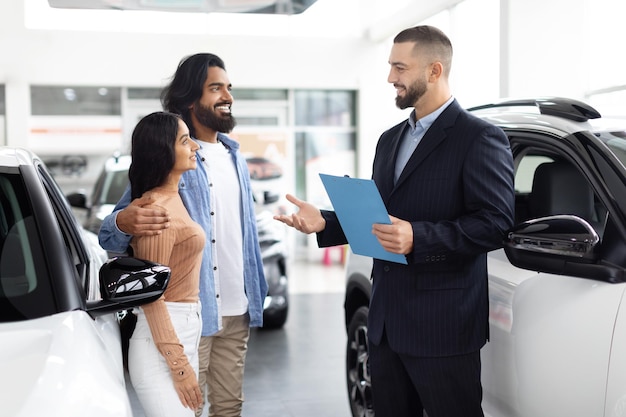 salesman chatting with eastern couple by a white car
