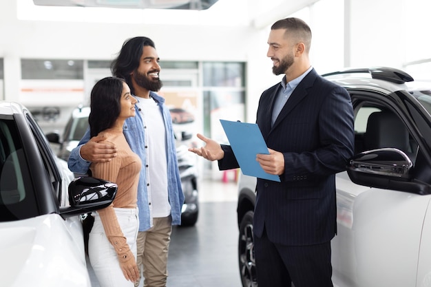 Photo salesman chatting with eastern couple by a white car