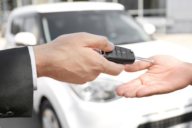 Salesman giving car key to customer outdoors